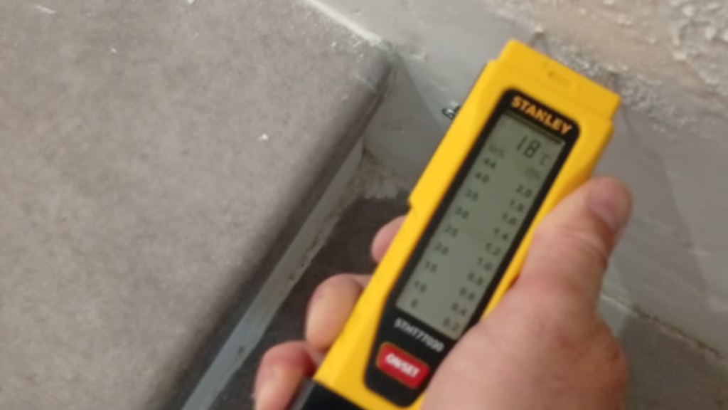 Moisture meter checking rising damp near a wall skirting board
